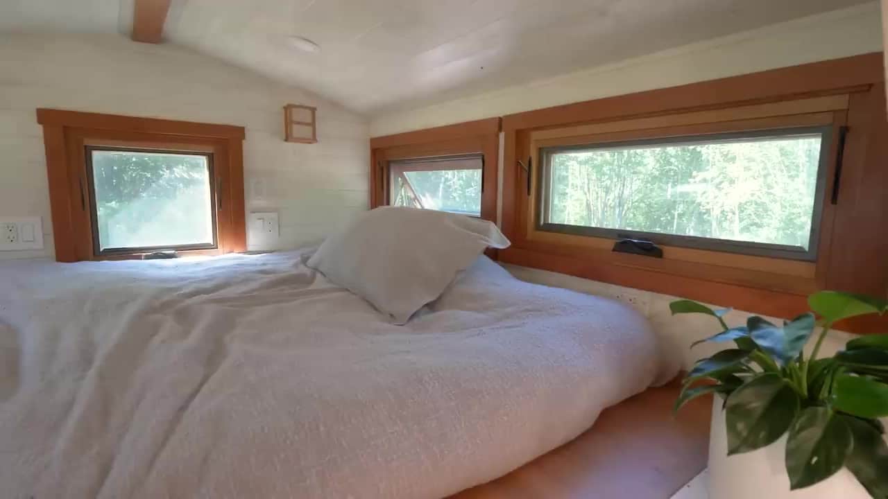 Loft bedroom with a bed and wood-framed windows looking into the trees