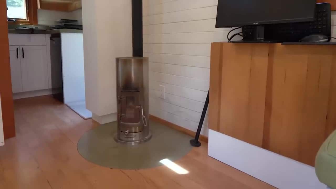 Cylindrical stainless wood stove on a circular flush concrete hearth