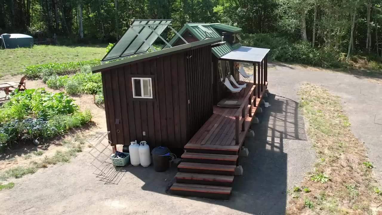 Workshop shed with a rooftop solar array, propane tanks, and a cedar deck connecting to the tiny house