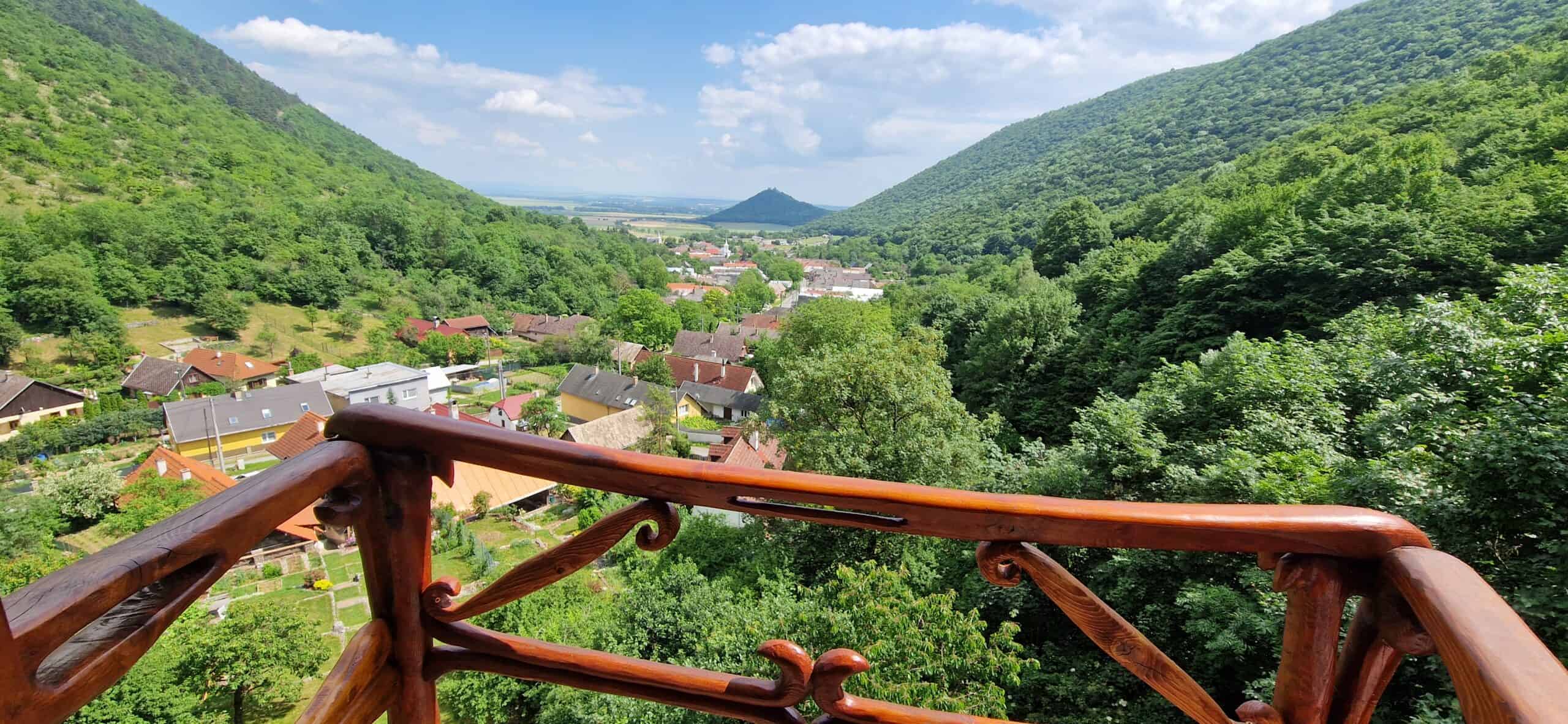 View from the tower balcony with handcrafted wooden railing overlooking the village of Háj and green hills