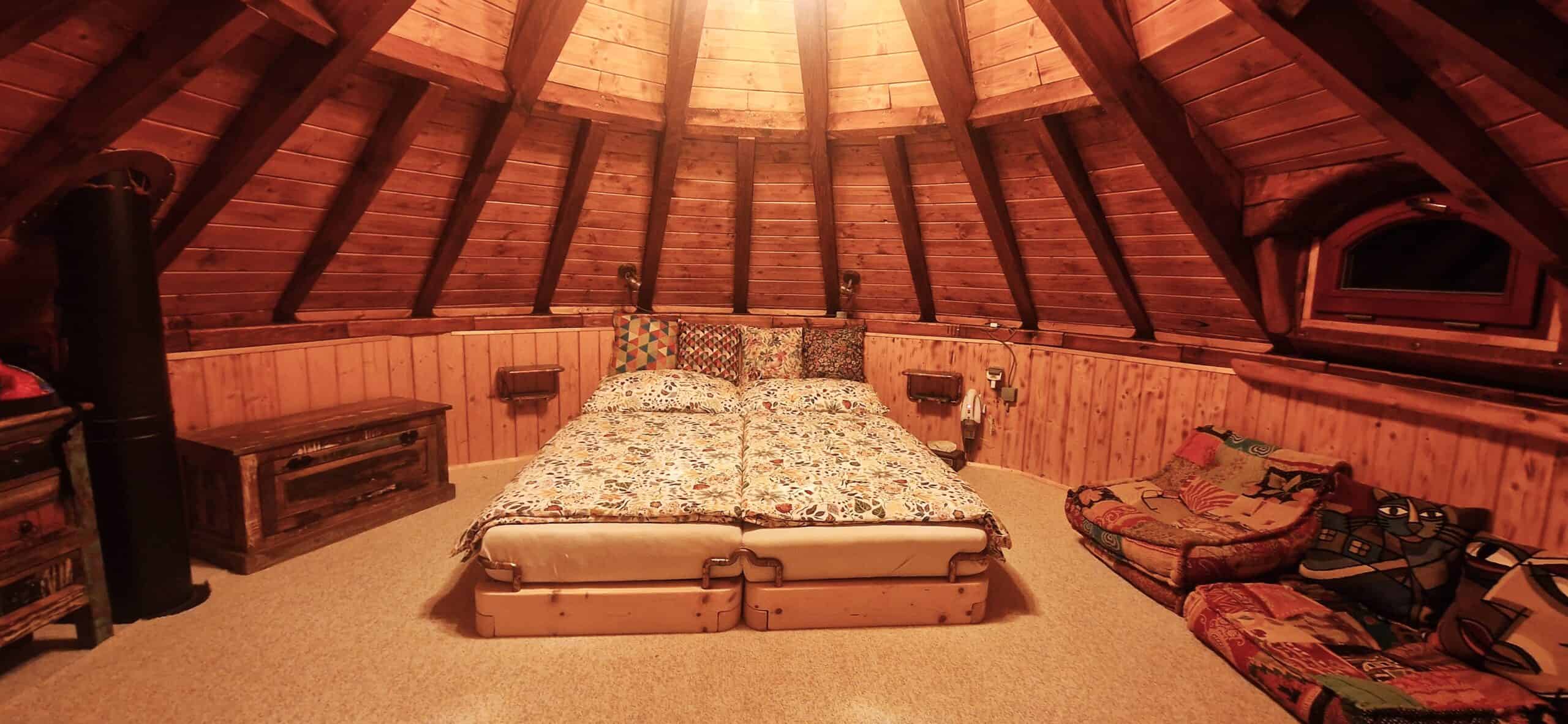 Circular tower bedroom under a vaulted timber roof with floral bedding and arched window