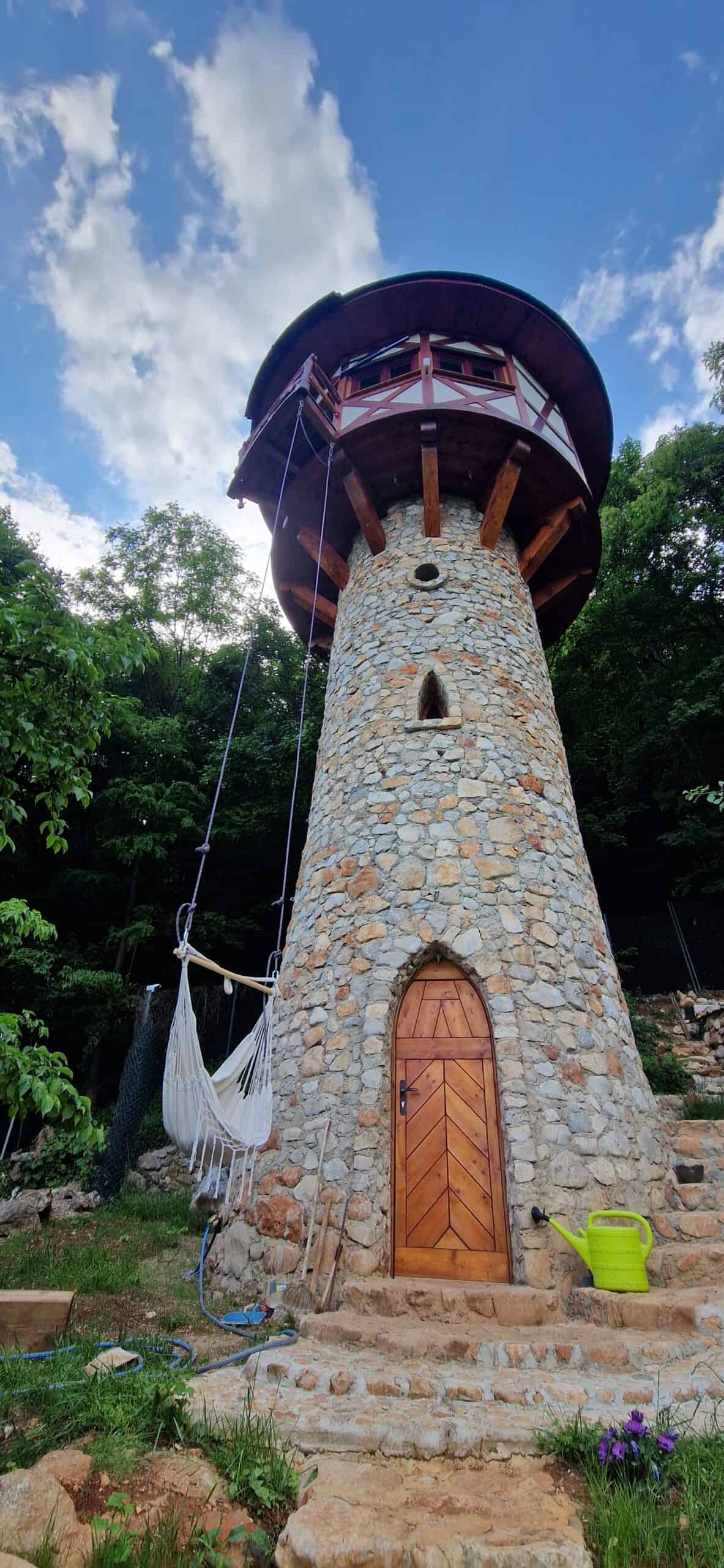 Low-angle view of the hand-built stone tower with timber-framed upper rooms and a hanging hammock