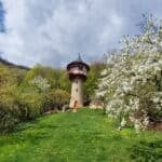 Tall stone fantasy tower with Tudor balcony and conical roof among spring blossoms in Háj, Slovakia