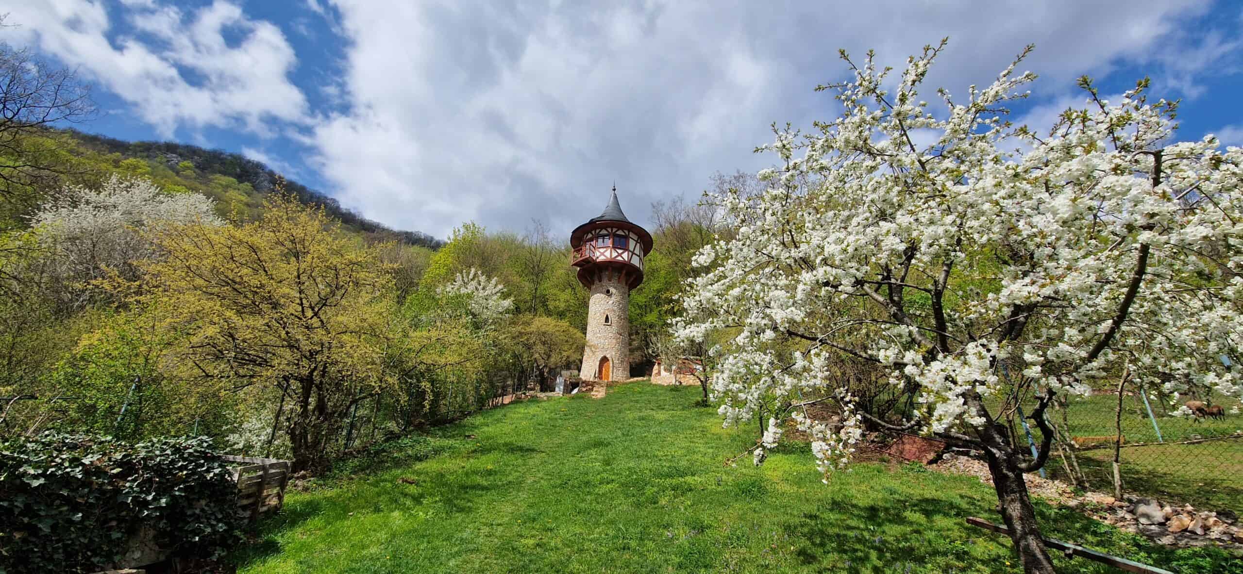 Tall stone fantasy tower with Tudor balcony and conical roof among spring blossoms in Háj, Slovakia