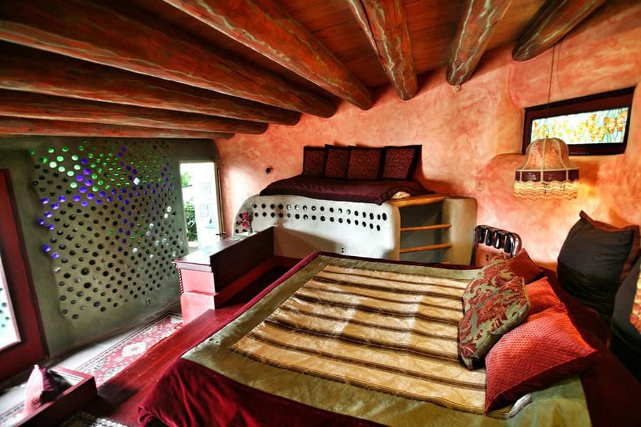 Bedroom with two beds, vigas, and a colored bottle wall