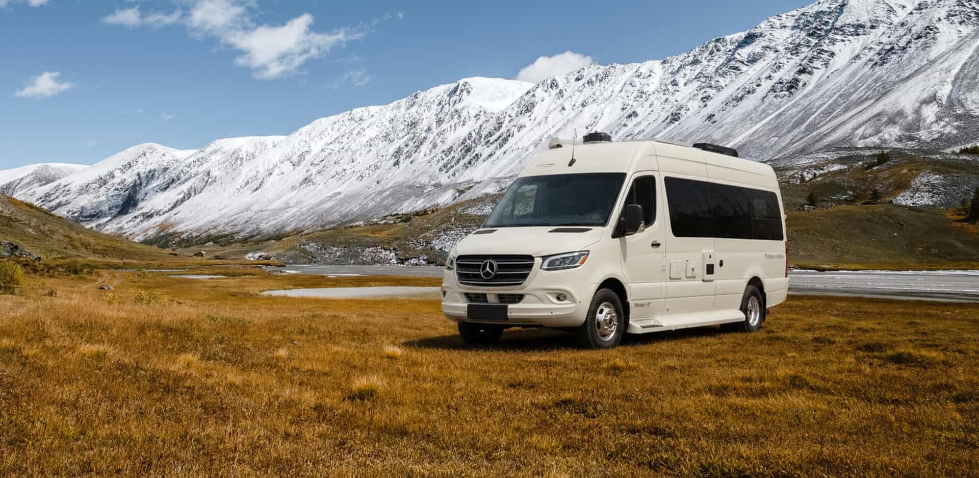 Cream Pleasure-Way Plateau TS parked on golden grassland below snow-covered mountains