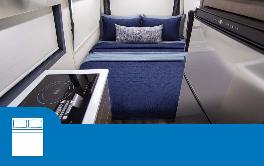 Rear queen bed made up with navy bedding, seen past the galley induction cooktop