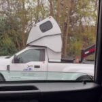 White Ford Super Duty hot-shot pickup with a compact cab-over sleeper pod, filmed from a Peterbilt — still from the Pless Trucking Facebook reel