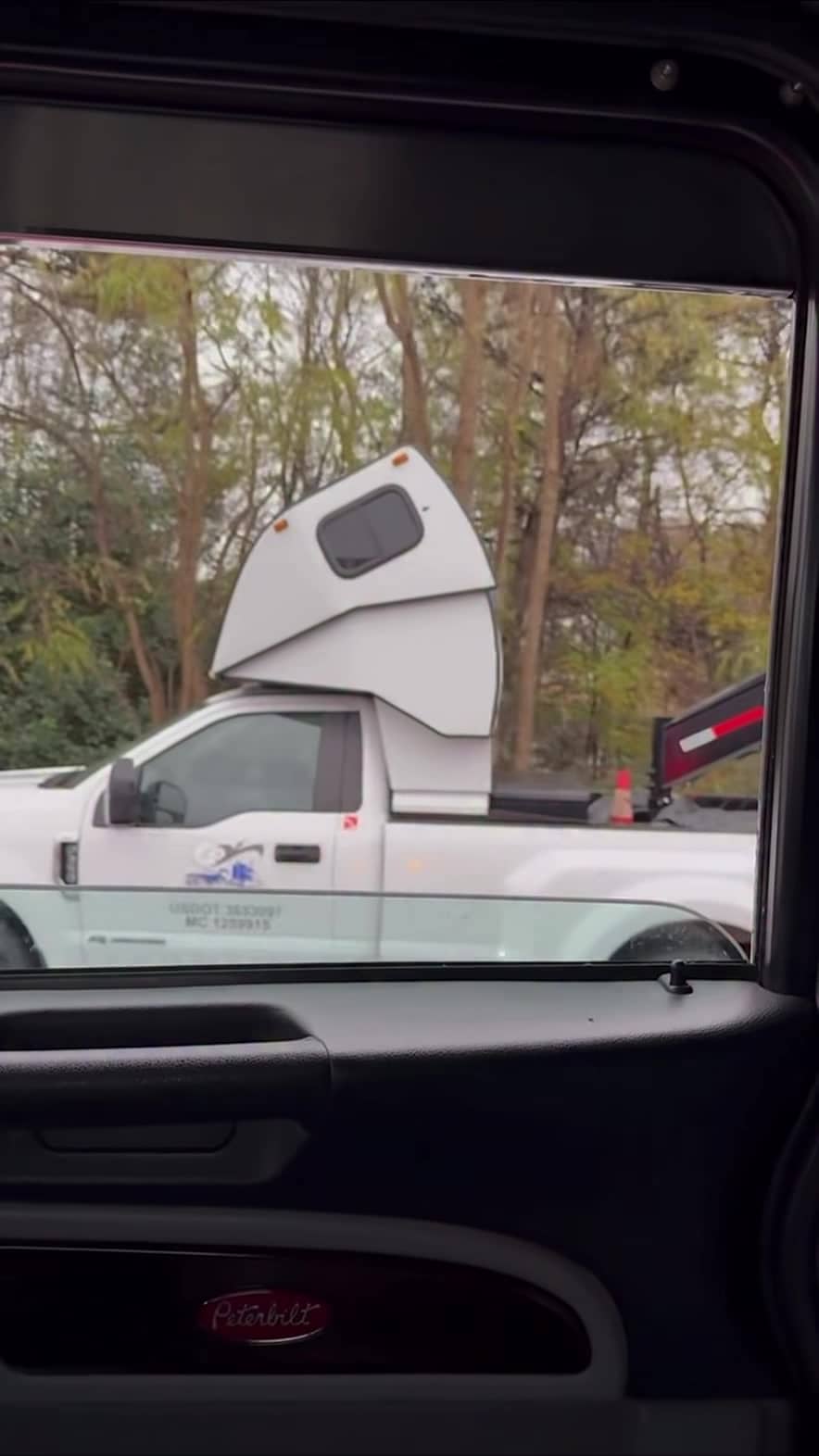 White Ford Super Duty hot-shot pickup with a compact cab-over sleeper pod, filmed from a Peterbilt — still from the Pless Trucking Facebook reel