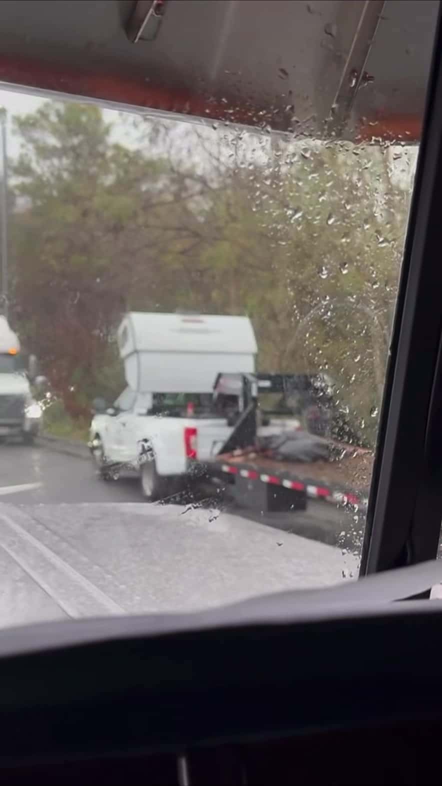 White pickup towing a black gooseneck flatbed with the sleeper sitting in the bed — still from the Pless Trucking reel