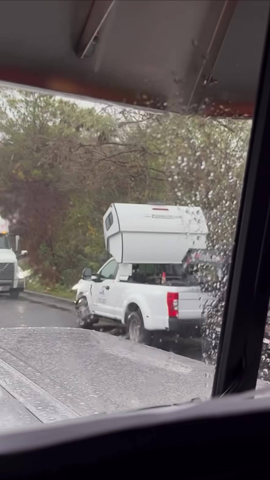 Rear of the cab-over sleeper on the white pickup, filmed through a wet windshield — still from the Pless Trucking reel