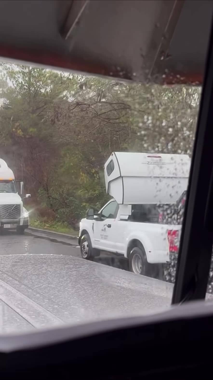 Wide rainy shot of the hot-shot pickup sleeper setup at a truck stop — still from the Pless Trucking reel