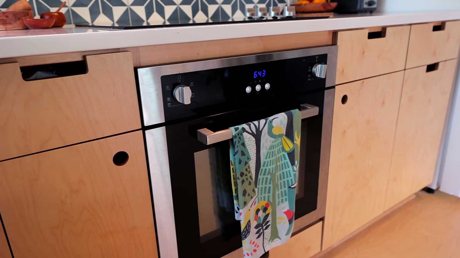 Close-up of Baltic birch plywood cabinet drawers with carved cutout pulls beside a built-in black wall oven