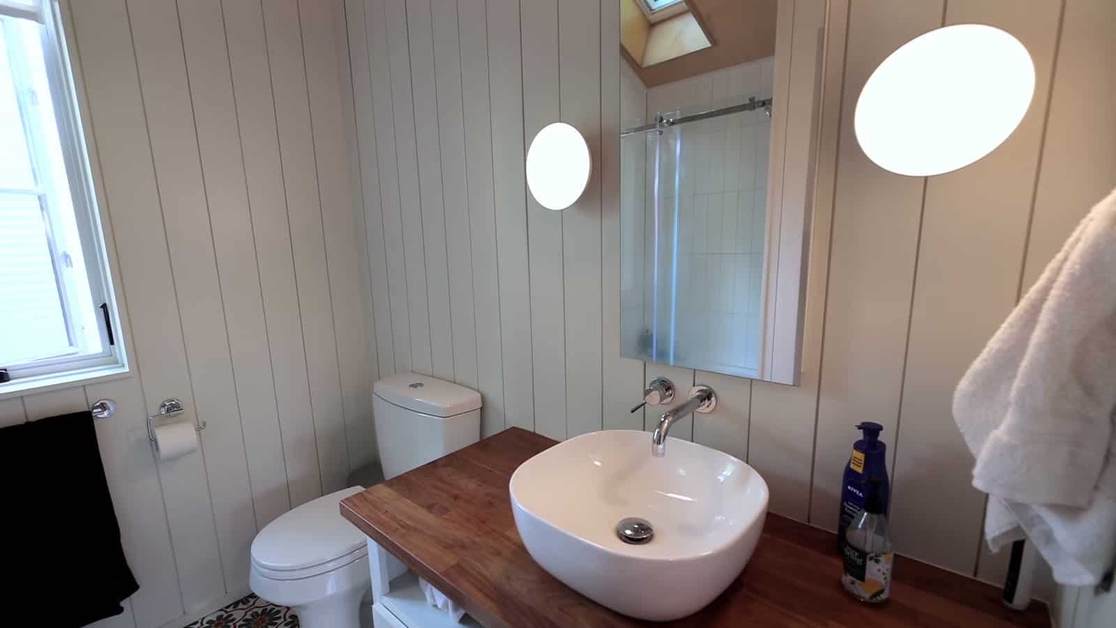 Small white bathroom with walnut vanity top, vessel sink, wall-mounted faucet, toilet, and a washer-dryer under a cabinet