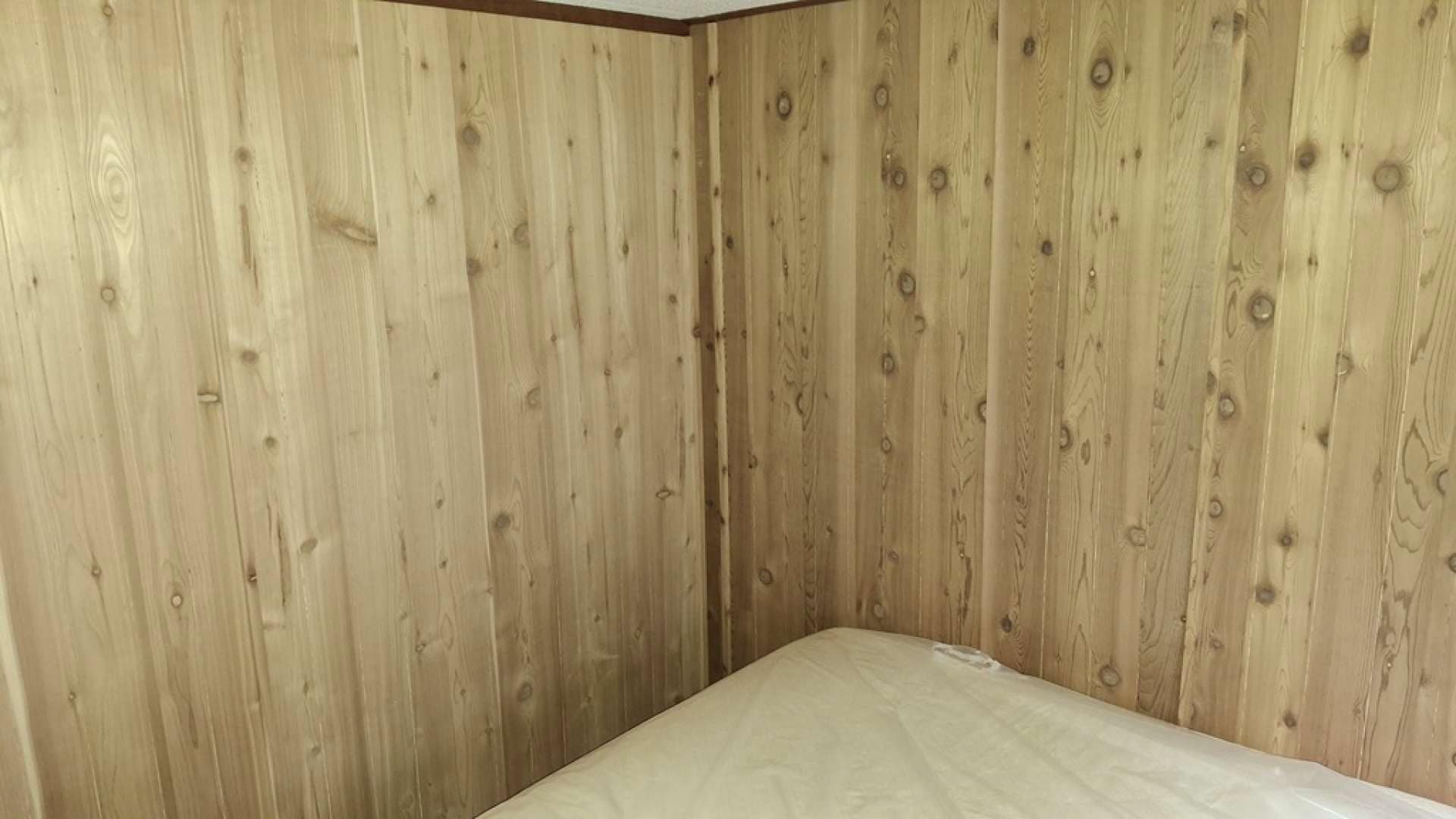 Close-up of vertical cedar wall panels meeting in a corner beside a mattress edge