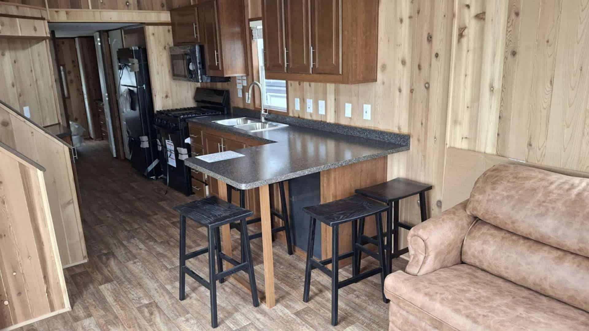 Cedar-paneled kitchen with an island bar, stools, black range, and loft stairs