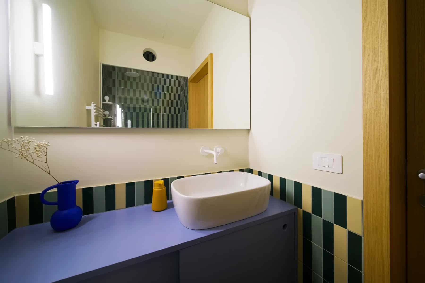 Bathroom with a wide blue vanity, white vessel sink, large mirror, and green and white tiles