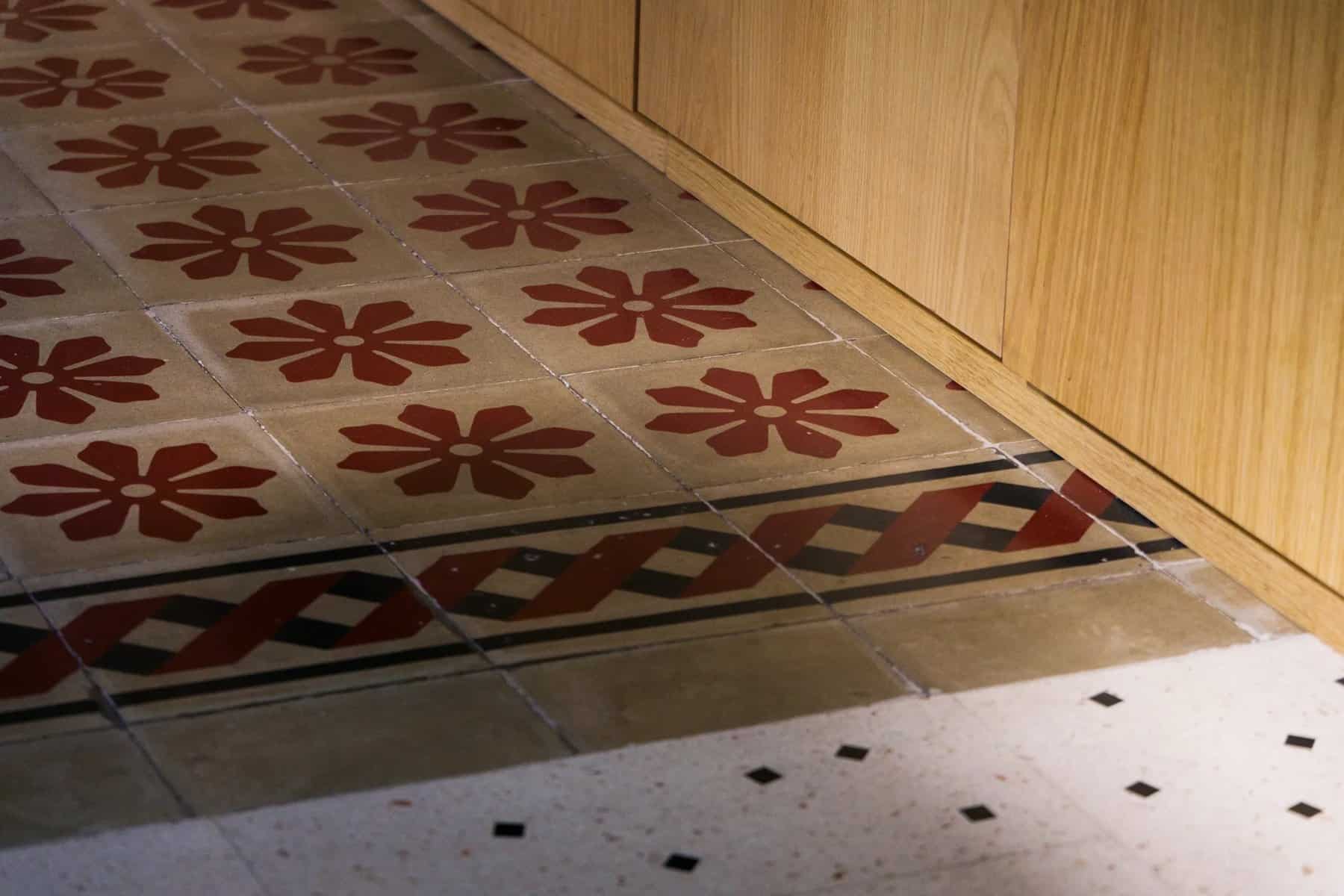 Original red and white patterned cementine tiles meeting new terrazzo-style tiles beside oak joinery