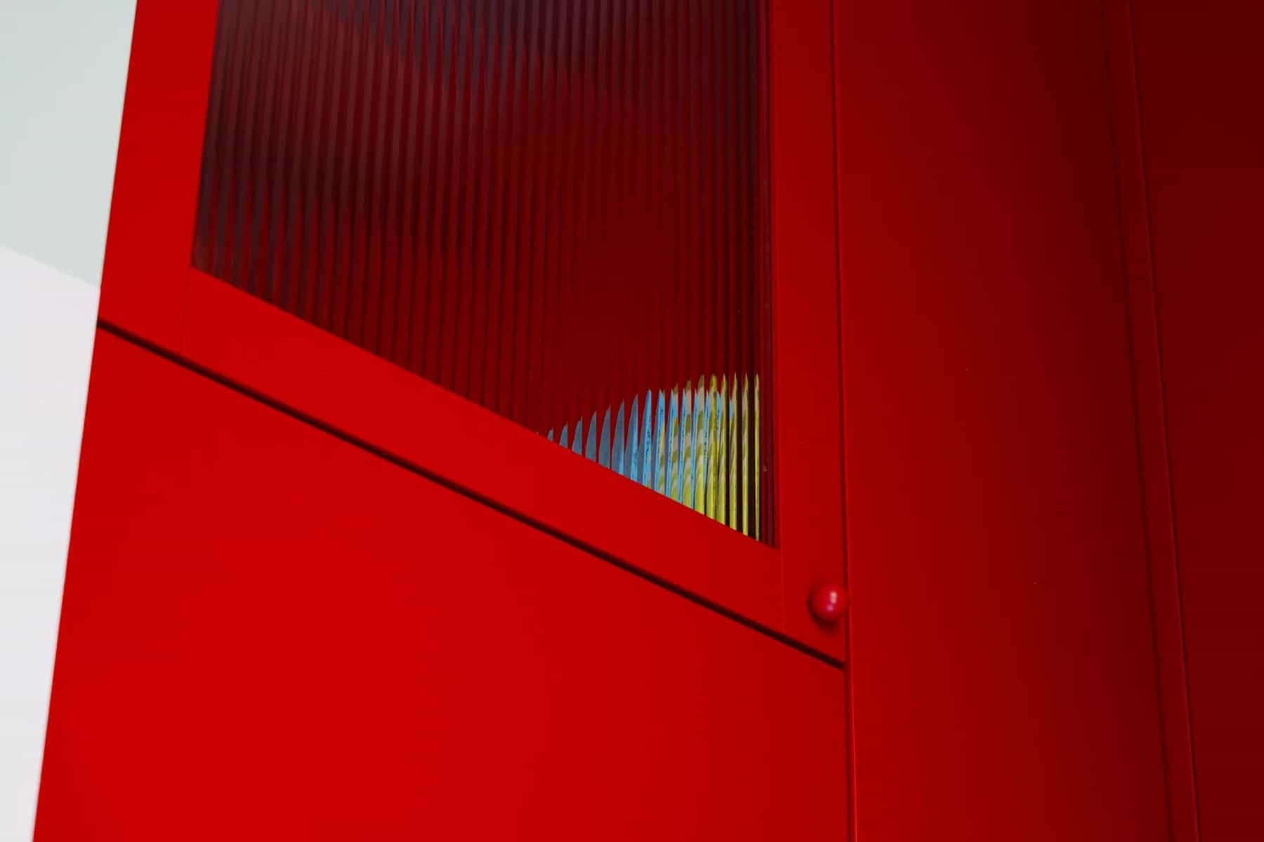 Fluted glass panel set into red kitchen cabinetry that passes light to the bathroom