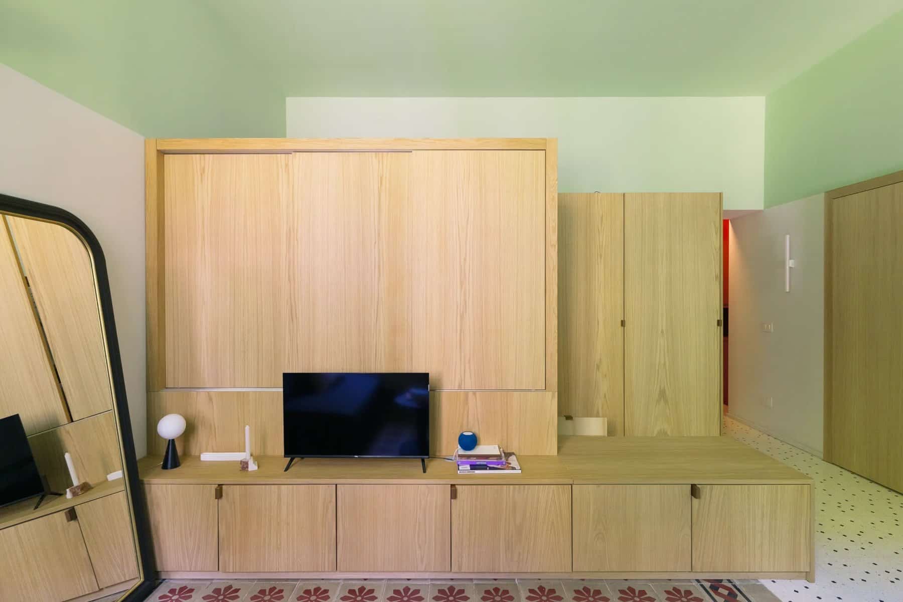 Oak sleeping alcove closed with sliding panels, low TV unit in front, in a Milan apartment