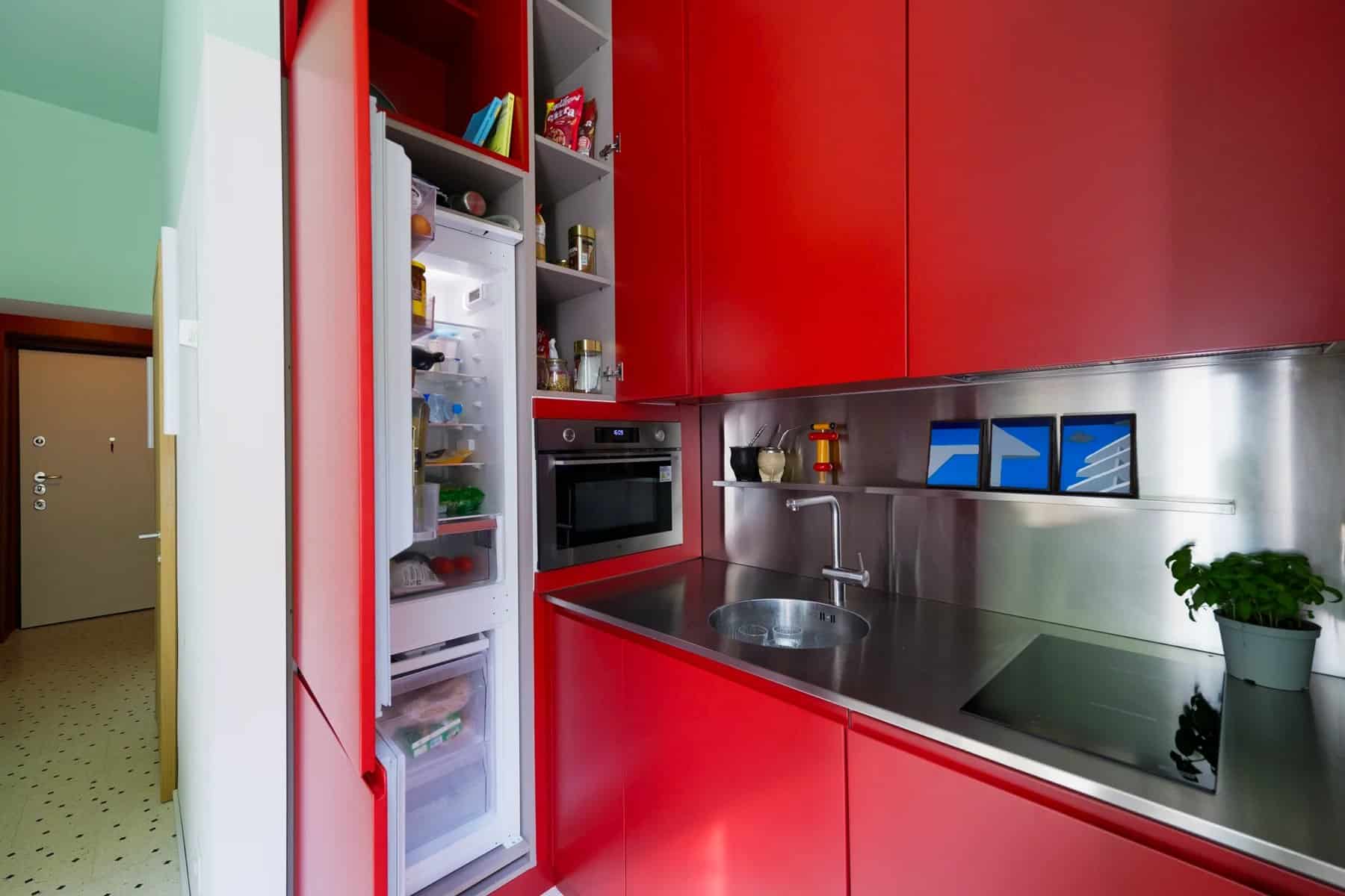 L-shaped kitchen with deep-red cabinets, stainless steel counter and backsplash, and a full-height fridge