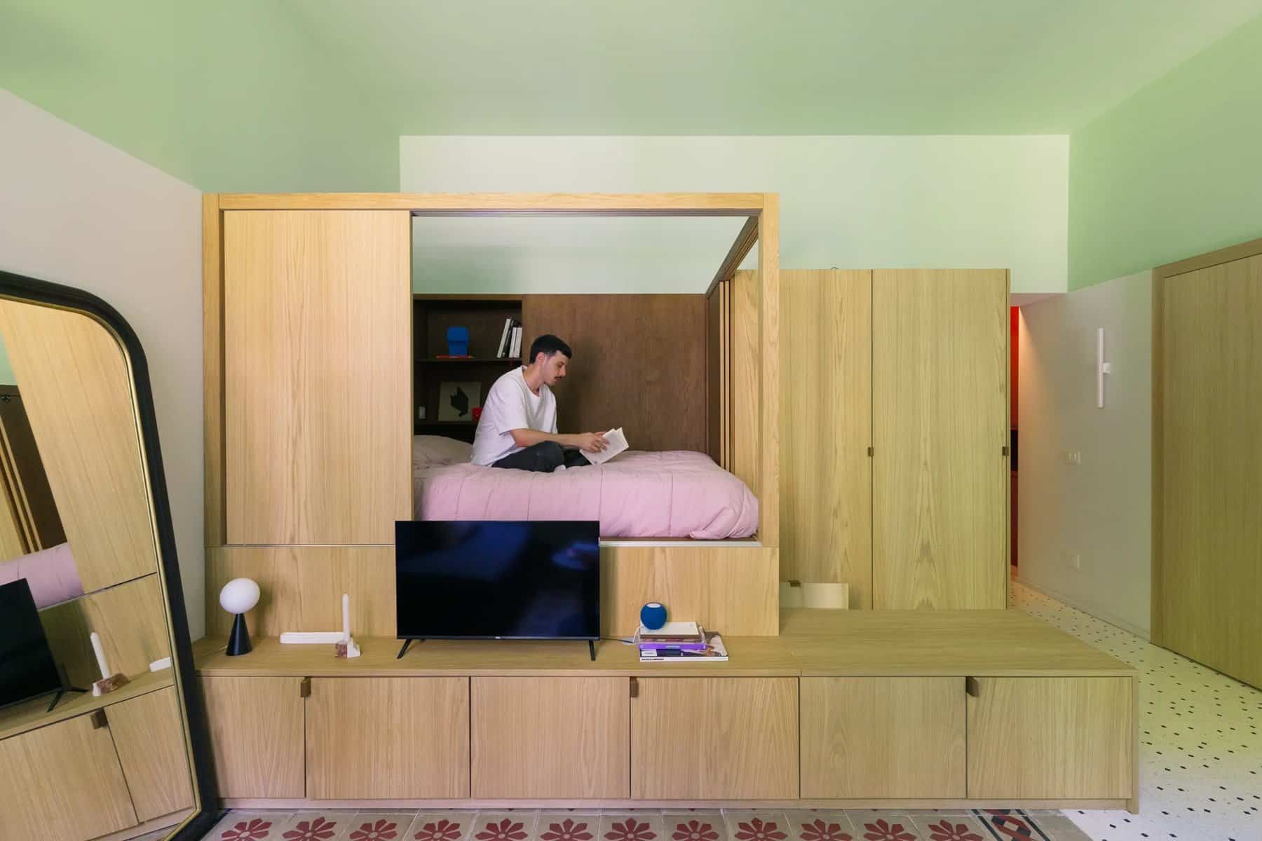 Oak sleeping alcove open, with a person reading on the bed above a low TV and storage unit