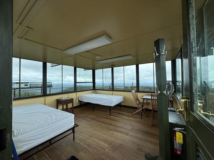 Cab interior with two twin cots, table and chairs, and wraparound windows at Red Oak Fire Lookout