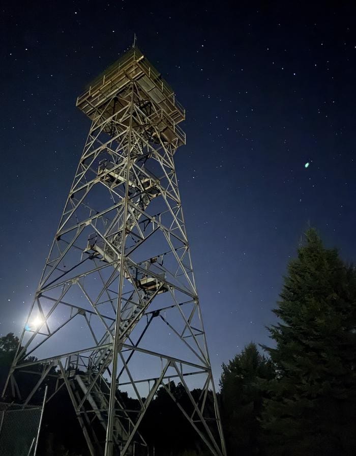 Wider night exterior of Red Oak Fire Lookout tower lit under stars over Webster County forest