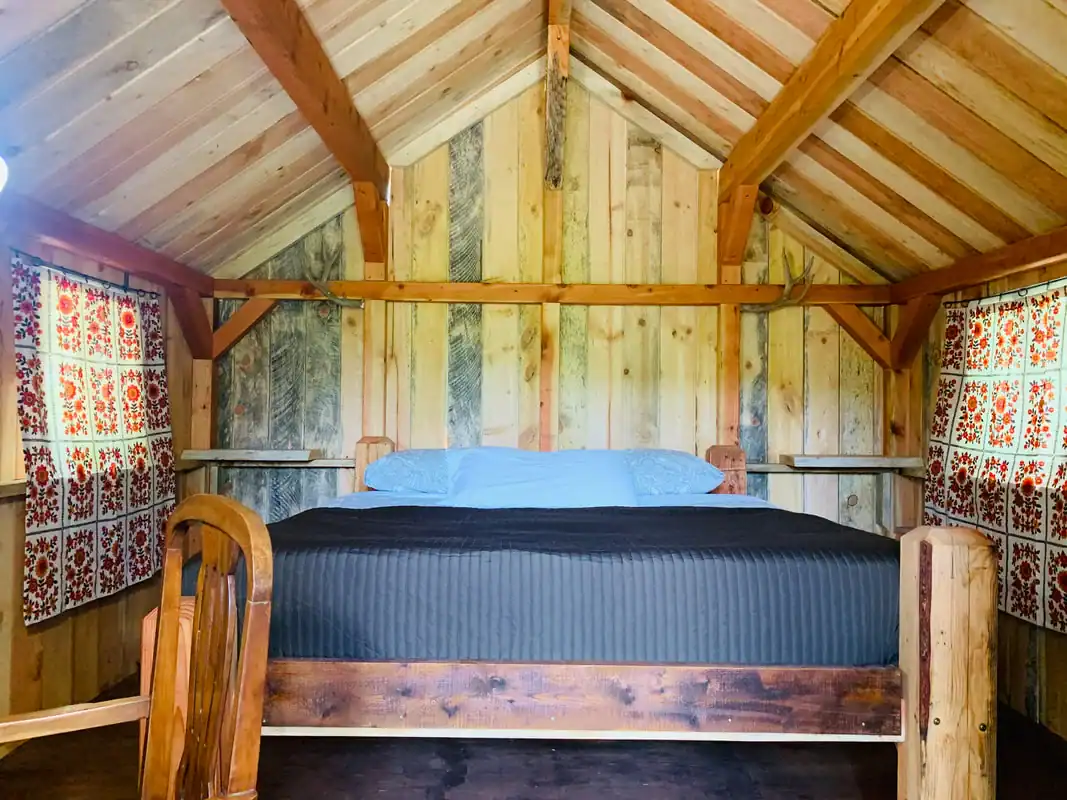 King bed head-on with antlers above, timber beams and salvaged wood walls