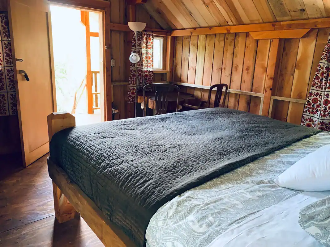 King bed and seating corner with the deck door open to green foliage