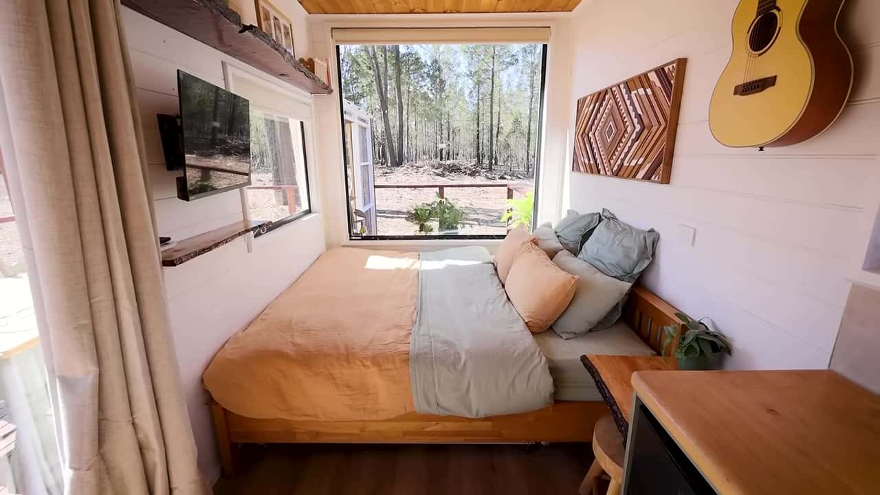King-size bed spanning the width of a shipping container, with a large picture window to the bush and geometric timber wall art