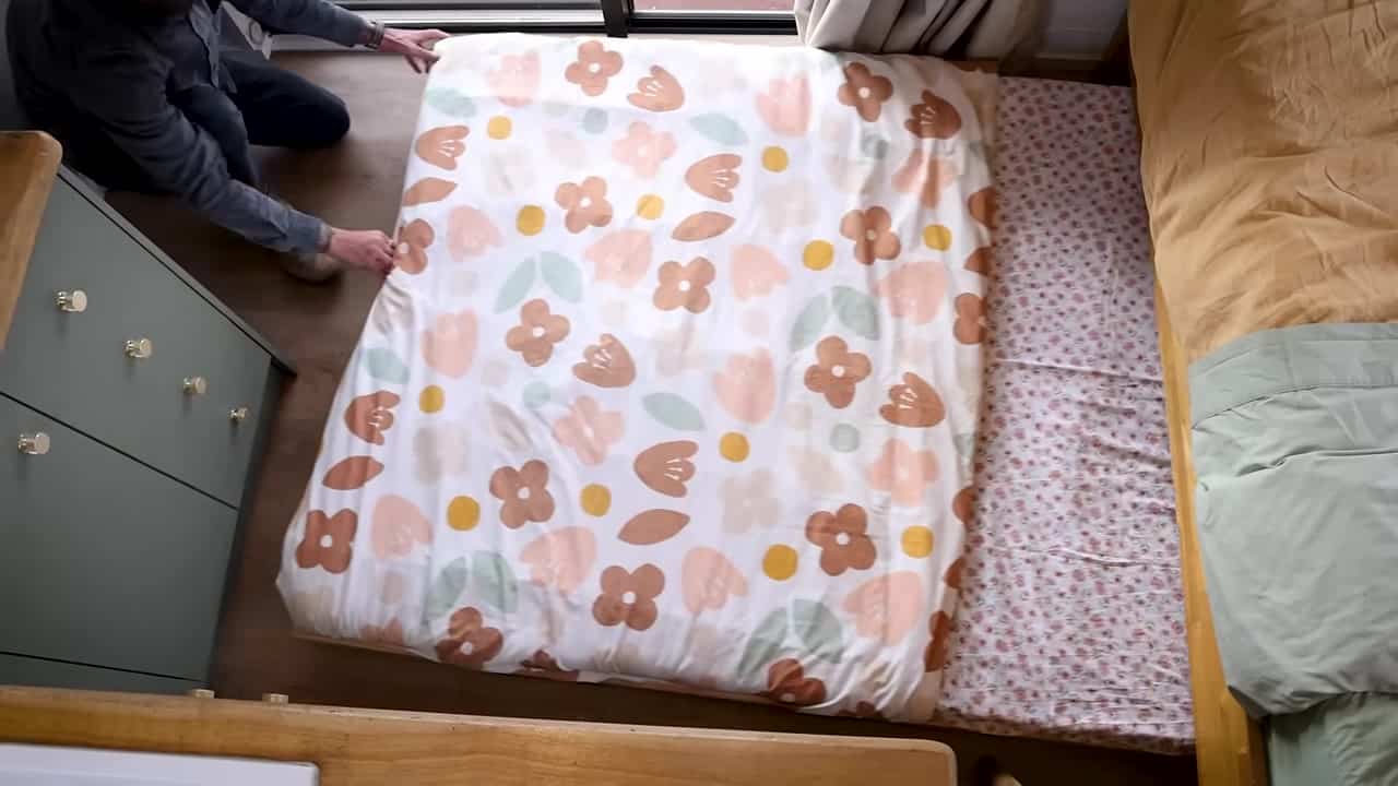 Floral slide-out kids bed on wheels being pulled from under a king bed in a compact shipping container home