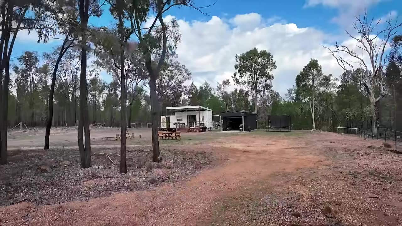 Wide view of a two-acre Queensland clearing with a white 20-ft container home, covered deck, charcoal shed, trampoline, and eucalyptus bush
