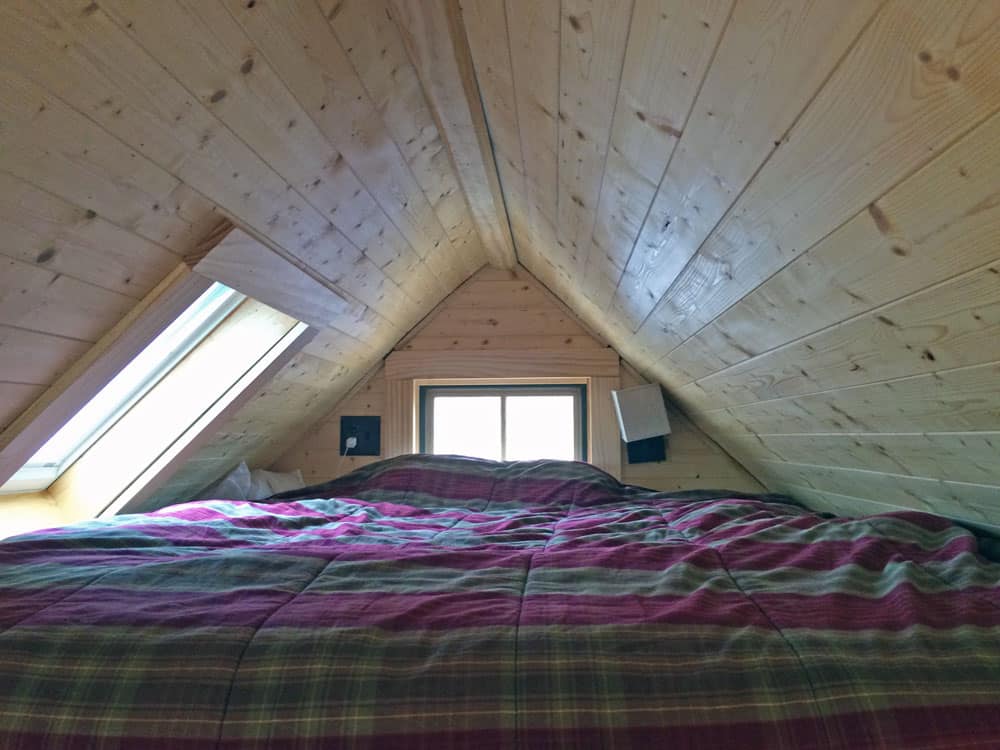 Sleeping loft with a queen bed, pine ceiling, skylight, and a small gable-end window