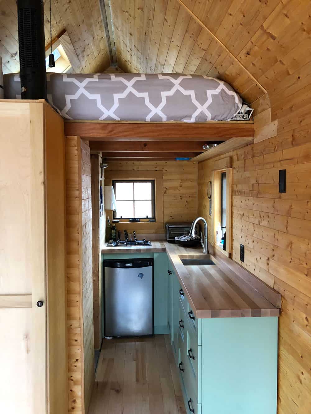 View from the front door down the length of the tiny house toward the kitchen, with the loft overhead