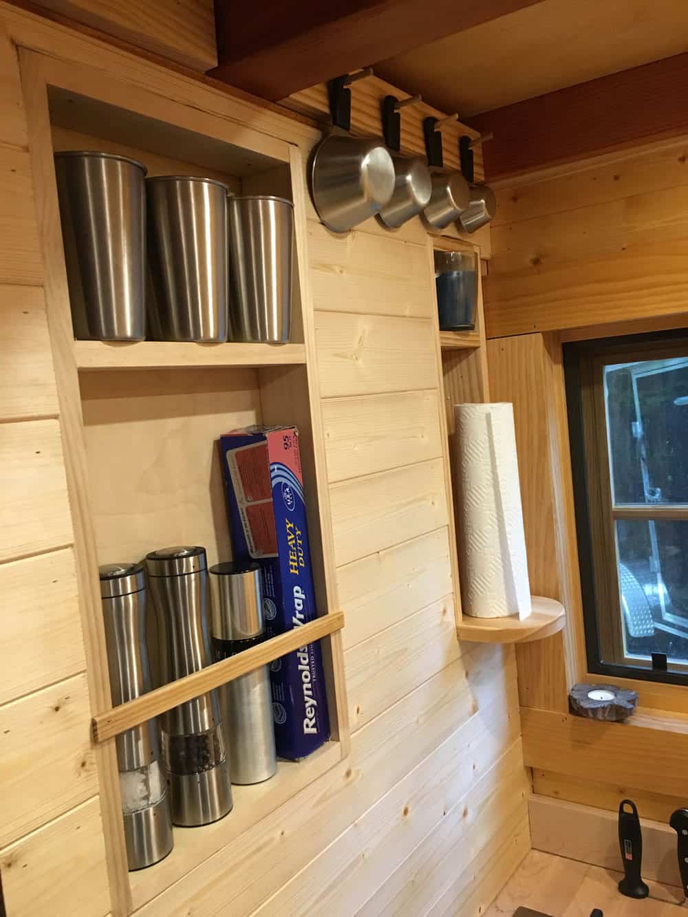 Recessed wall niche between the studs holding canisters, foil, and paper towels, with pots hanging above