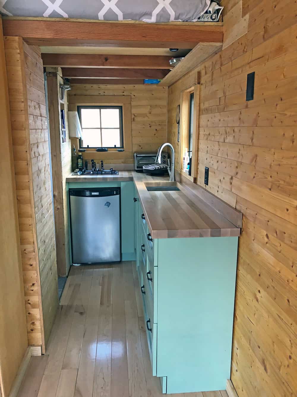 Galley kitchen with mint-green cabinets, butcher block counters, an under-counter fridge, and the sleeping loft above