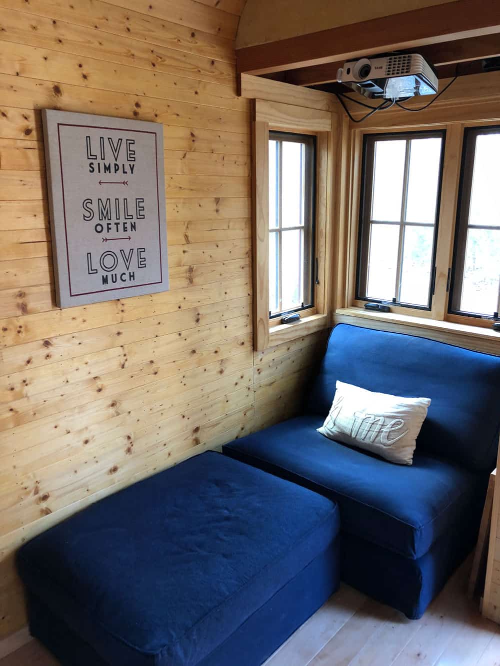 Front nook with a navy blue chair and ottoman, pine walls, windows, and a ceiling-mounted projector