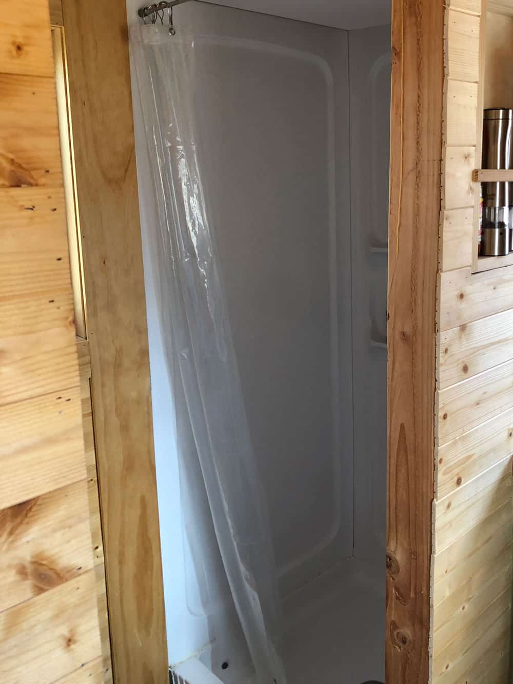 32-inch shower stall with a white curtain between pine walls