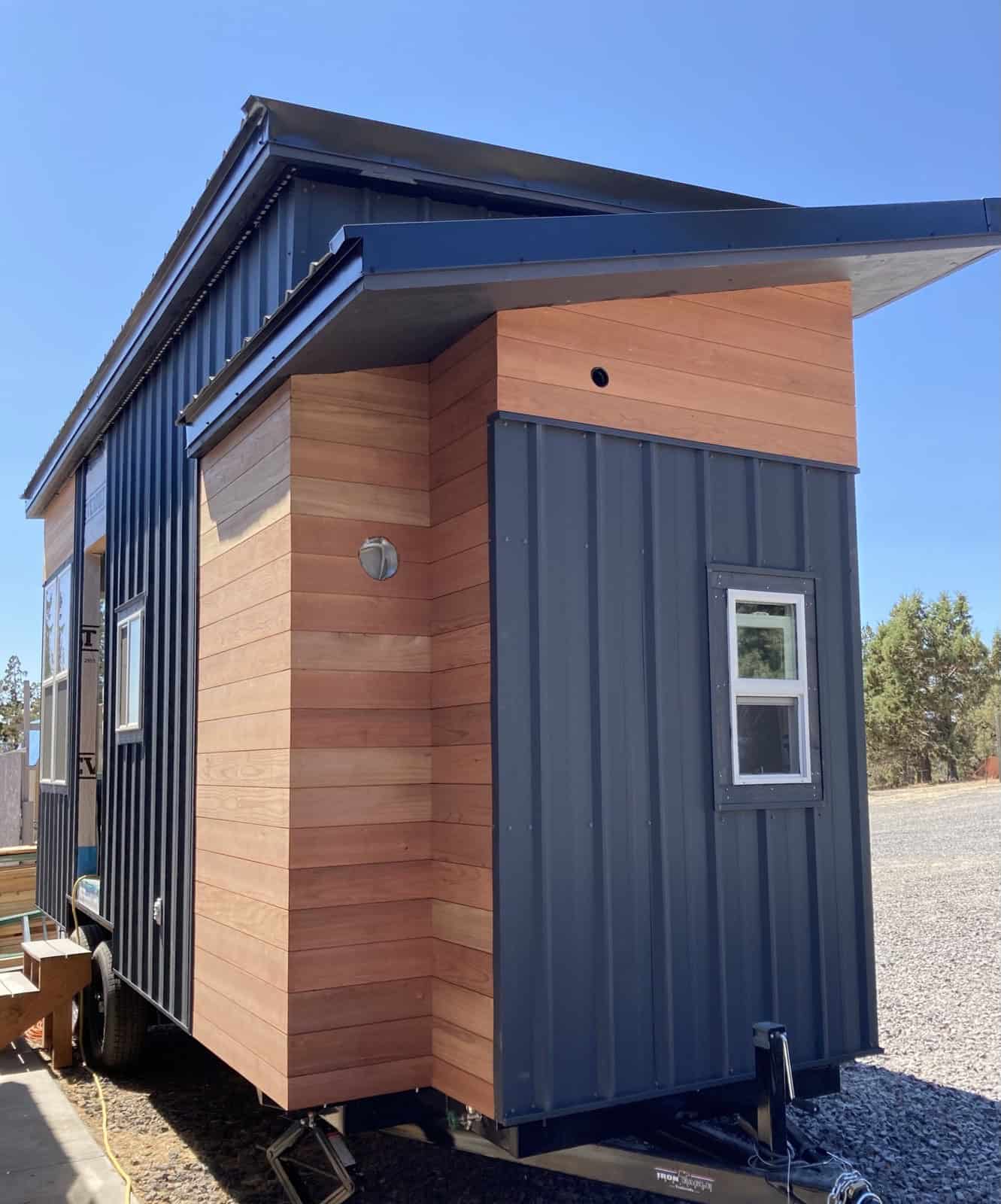 Corner of a tiny house with horizontal cedar siding meeting dark vertical siding under a projecting metal roof overhang