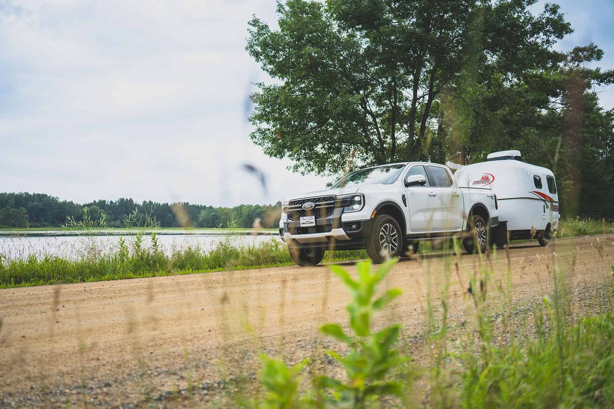 White pickup and a short Scamp on a dirt road by water