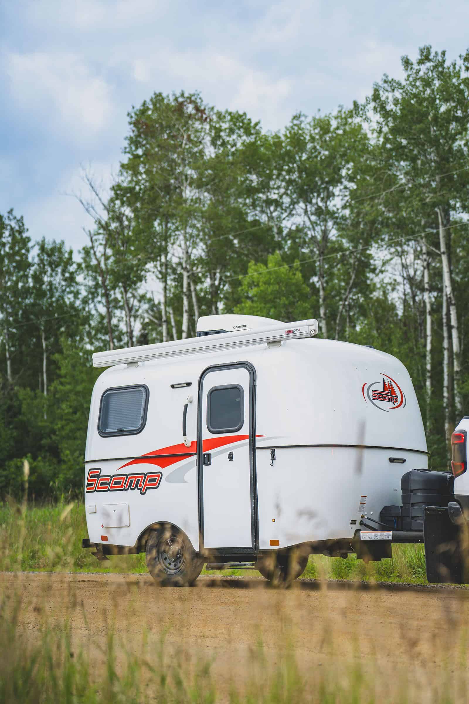 Side of a short white Scamp with an awning, birch trees behind