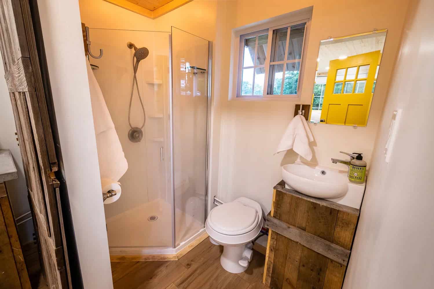 Container cabin bathroom with corner glass shower, toilet, and vessel sink on a wood vanity