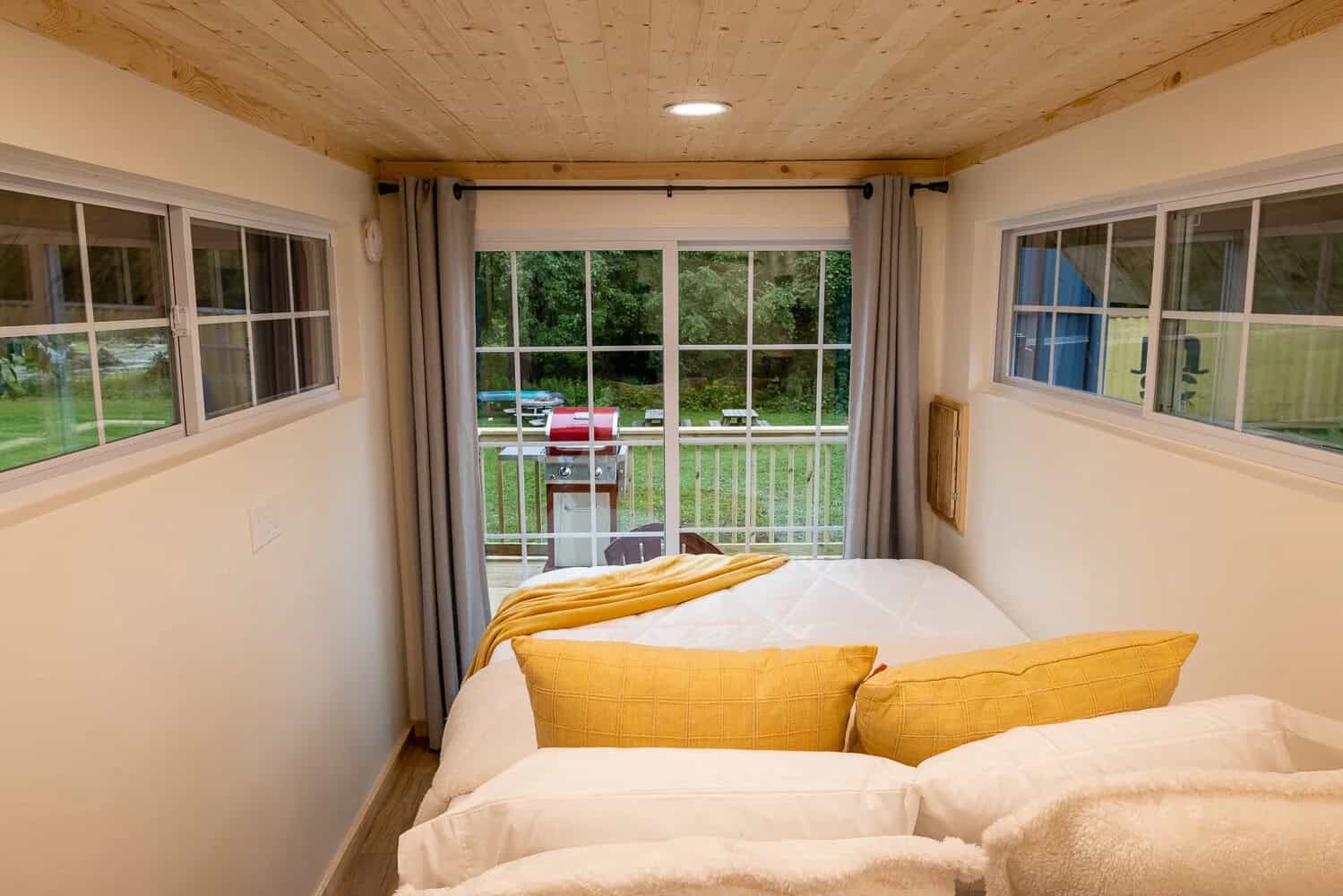 Queen bed with yellow pillows facing sliding glass doors in a container cabin