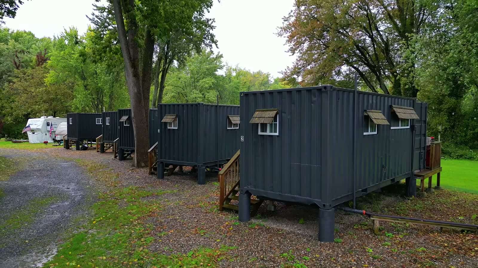 Shipping container cabin raised on concrete piers with wood stairs and a side deck