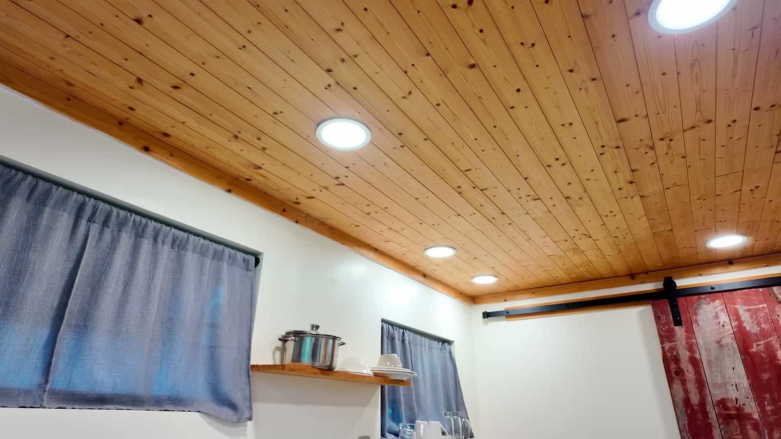 Tongue-and-groove pine ceiling with recessed lights and a red barn door in a container cabin