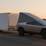 Electric vehicle towing a tiny house trailer on highway at sunset.
