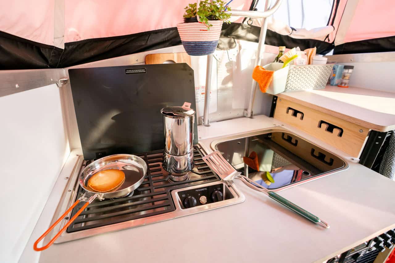 Compact tiny house kitchen with stove, utensils, and storage.