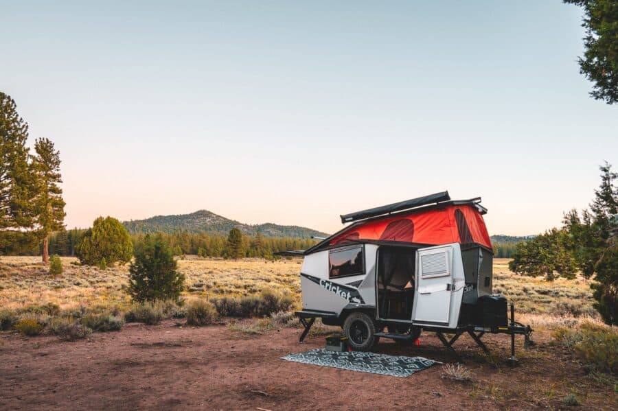 Compact tiny house on wheels with red roof in open landscape at sunset.