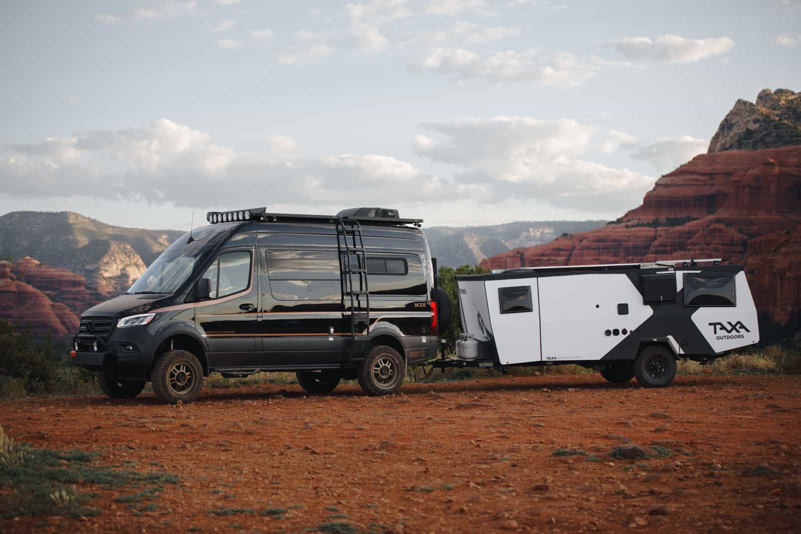 Compact tiny house with a trailer, parked in a desert with red rock formations in the background.